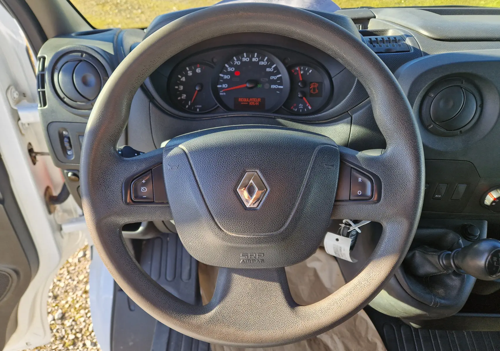 Vue intérieure centrée sur le volant noir du Renault Master blanc, avec tableau de bord et levier de vitesse manuelle visibles.