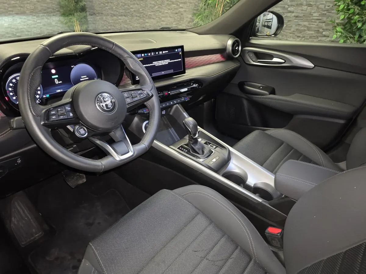Vue intérieure côté conducteur de l'Alfa Romeo Tonale gris, avec volant sport cuir et tableau de bord digital.