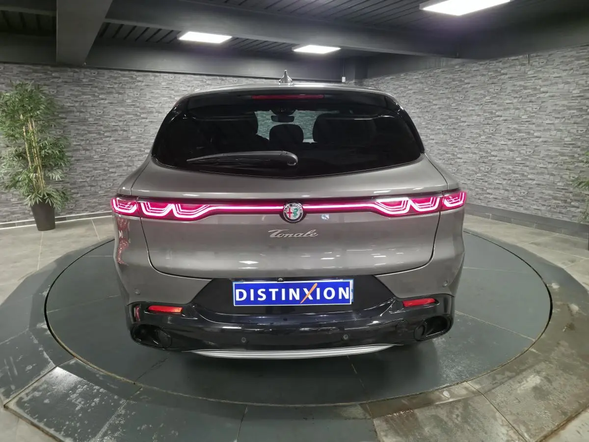 Vue arrière d'une Alfa Romeo Tonale gris métallisé avec feux LED allumés et logo central dans un showroom.