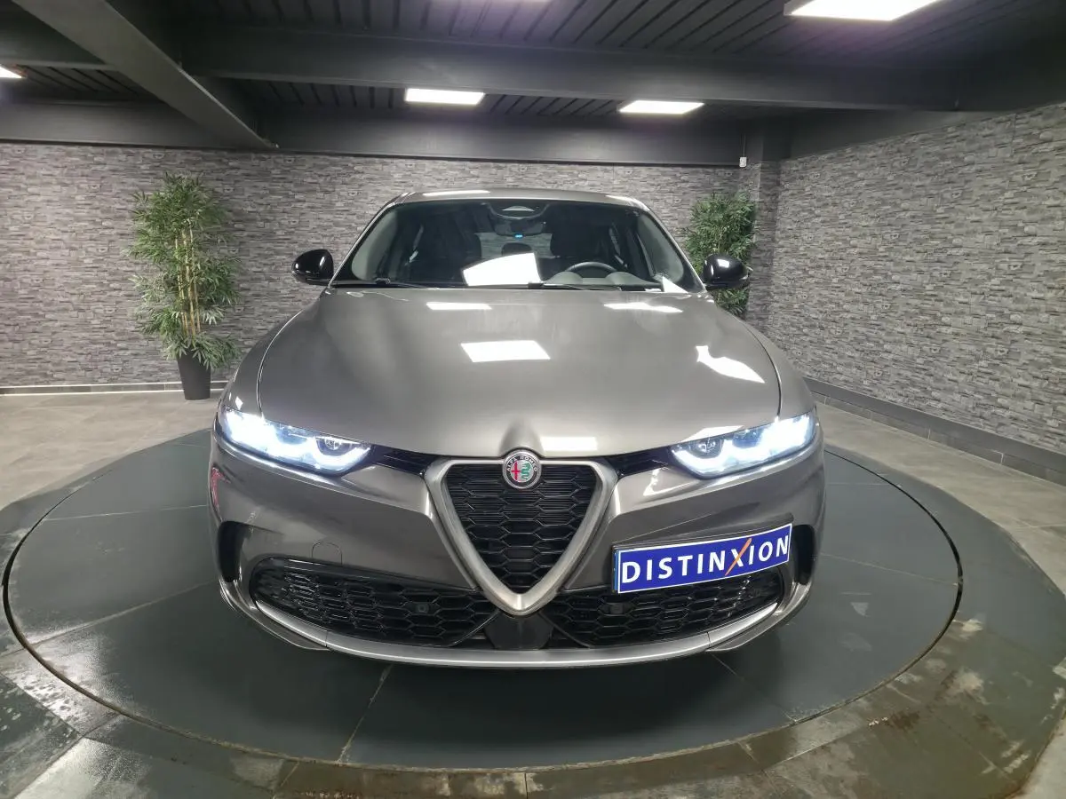 Vue avant d'une Alfa Romeo Tonale 1.3 PHEV gris métallisé avec phares LED allumés en intérieur showroom.