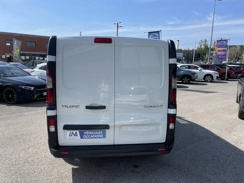 Vue arrière d’un Renault Trafic Fourgon blanc L1H1, avec portes battantes fermées et logo visible, stationné en extérieur.