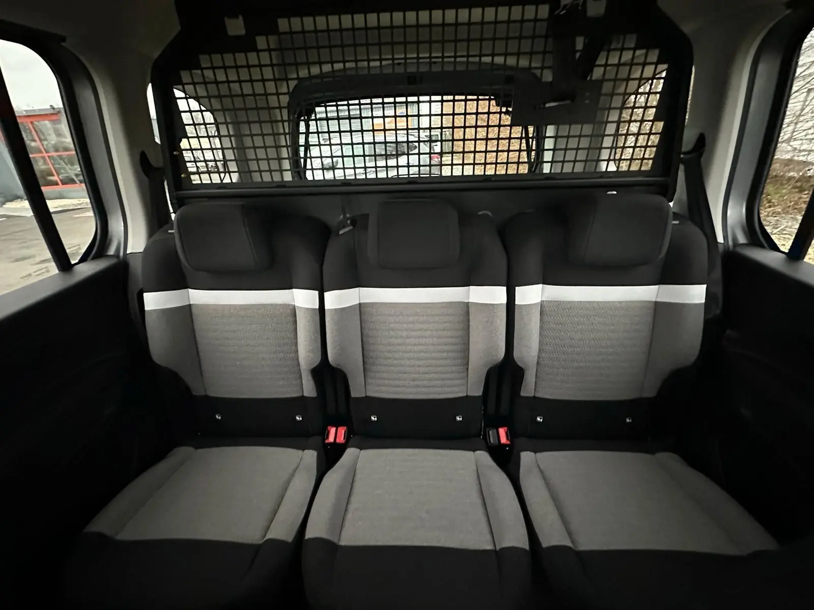 Vue intérieure arrière du Citroën Berlingo gris Artense, montrant les trois sièges passagers avec séparation grillagée.