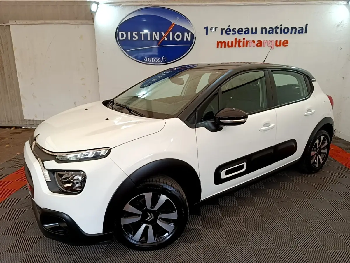 Citroën C3 blanche vue 3/4 avant droit, avec protections latérales noires et jantes alliage distinctives.