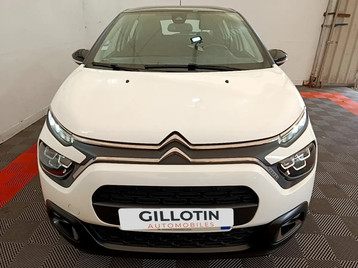 Vue frontale d'une Citroën C3 blanche avec calandre noire et feux LED distinctifs, stationnée en intérieur.