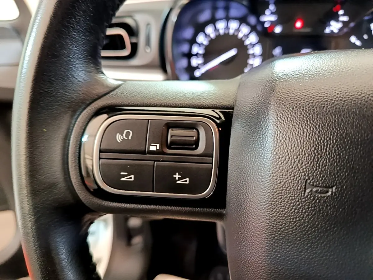 Gros plan sur le volant cuir noir de la Citroën C3 2021 avec commandes multifonctions et tableau de bord lumineux flou.