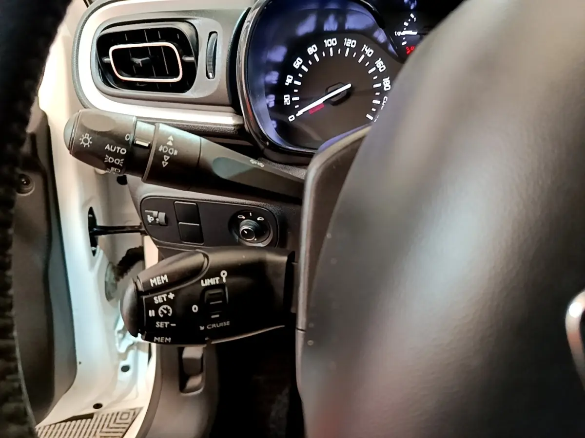 Vue intérieure côté conducteur de la Citroën C3 blanche, volant cuir et commandes au volant visibles avec tableau de bord éclairé.