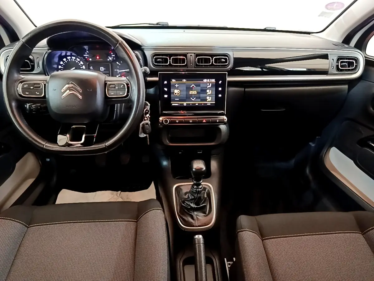 Vue intérieure avant du tableau de bord d'une Citroën C3 blanche, volant cuir multifonctions et écran tactile central allumé.