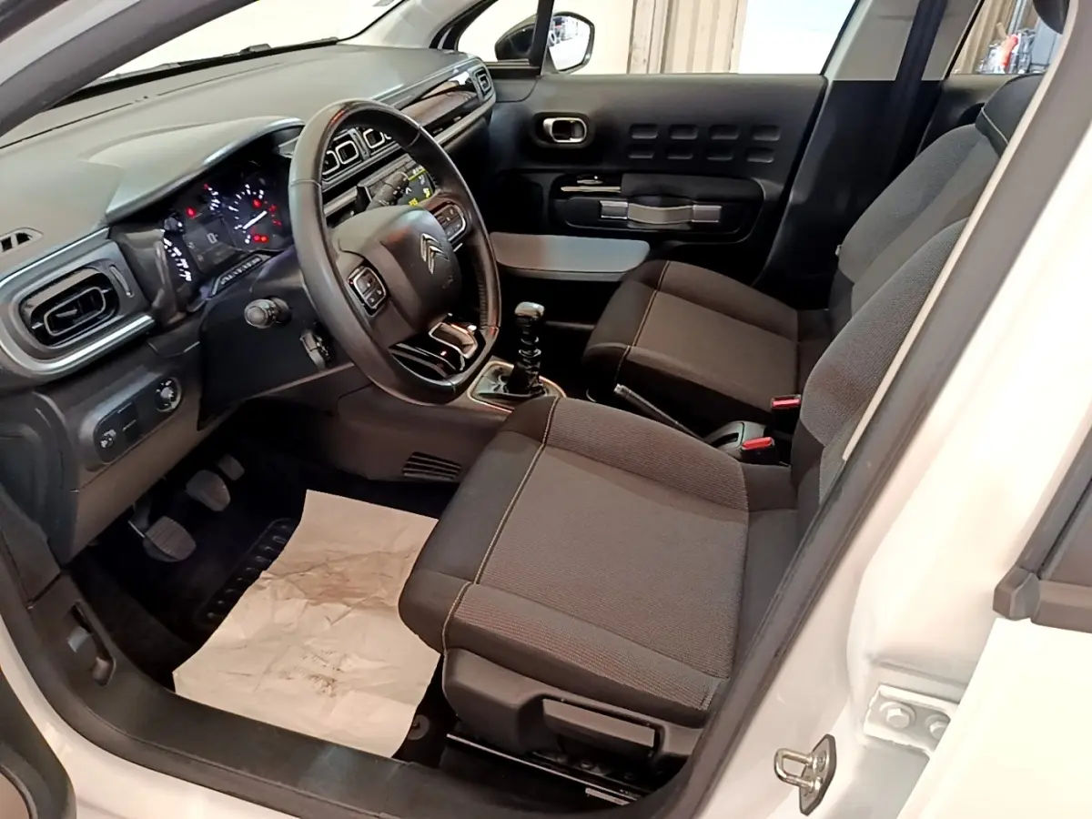 Vue intérieure côté conducteur de la Citroën C3 blanche 2021, volant cuir multifonctions et sièges tissu gris.