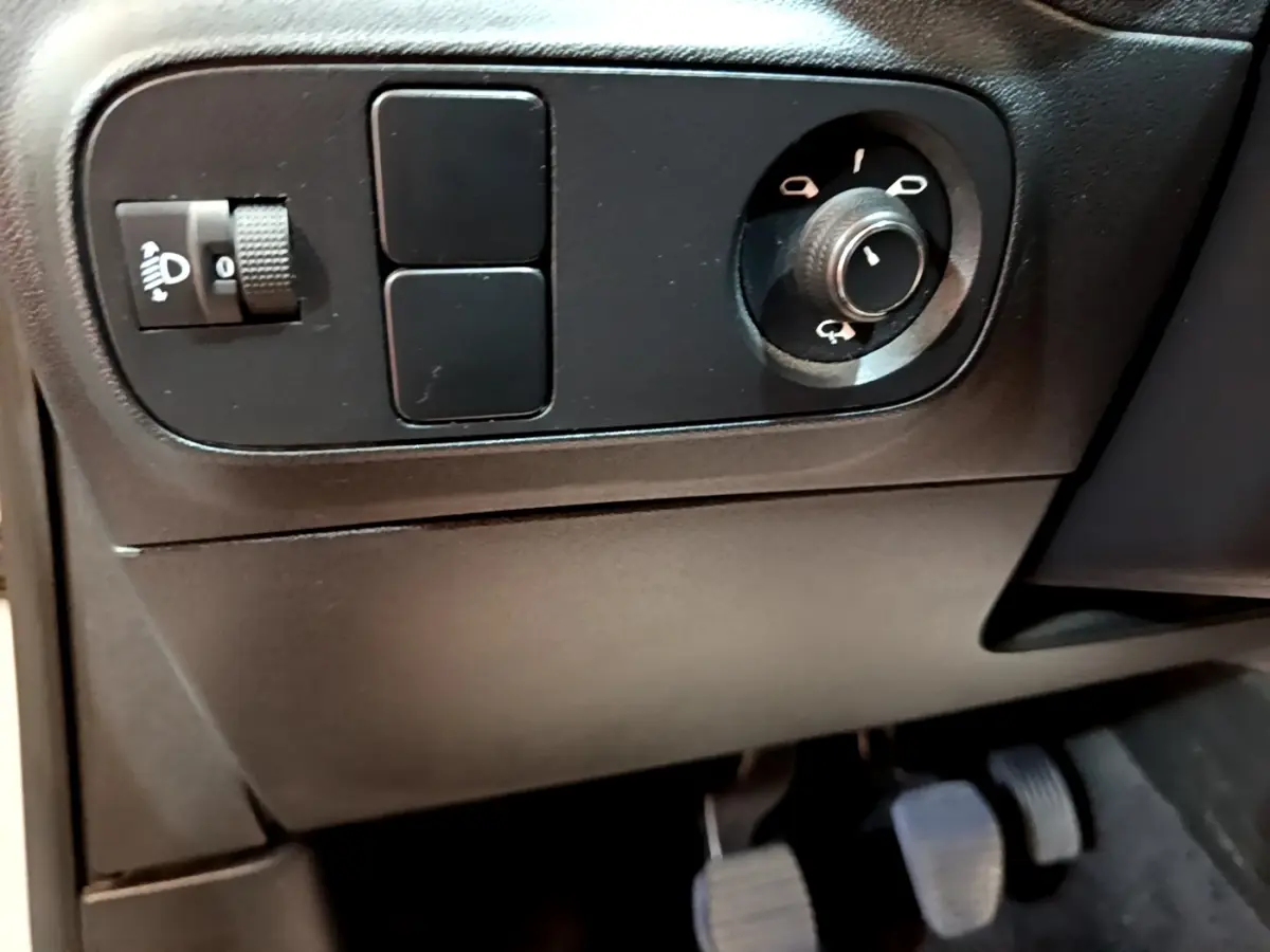 Détail du panneau de commandes côté conducteur avec réglage des phares et commande des rétroviseurs dans une Citroën C3 blanche.