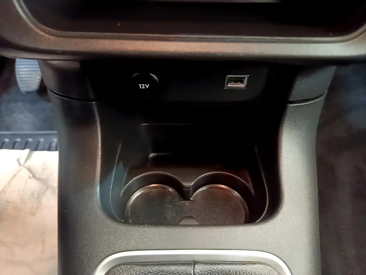 Gros plan sur la console centrale noire de la Citroën C3, montrant prise 12V, port USB et porte-gobelets.