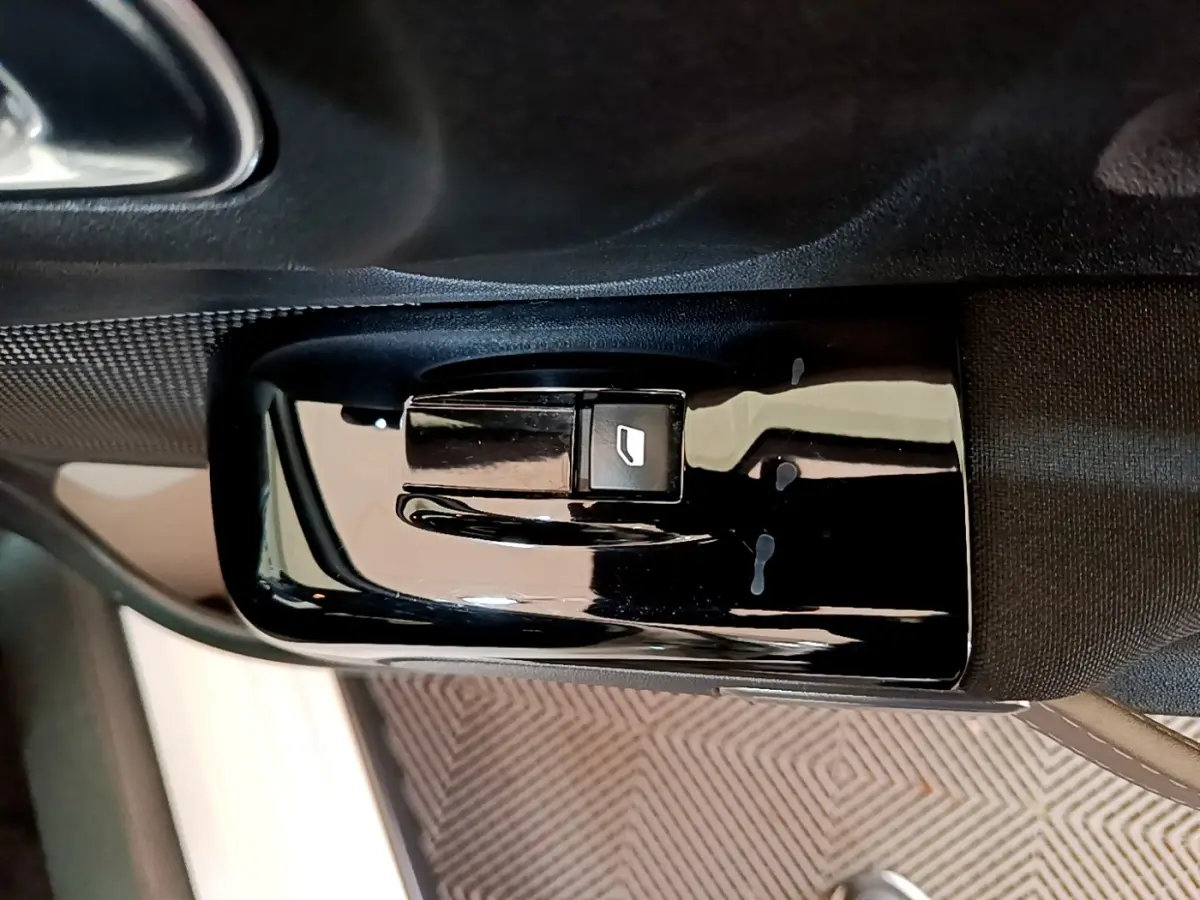 Gros plan sur le bouton de commande de la vitre électrique côté conducteur dans l'habitacle noir d'une Citroën C3 blanche.