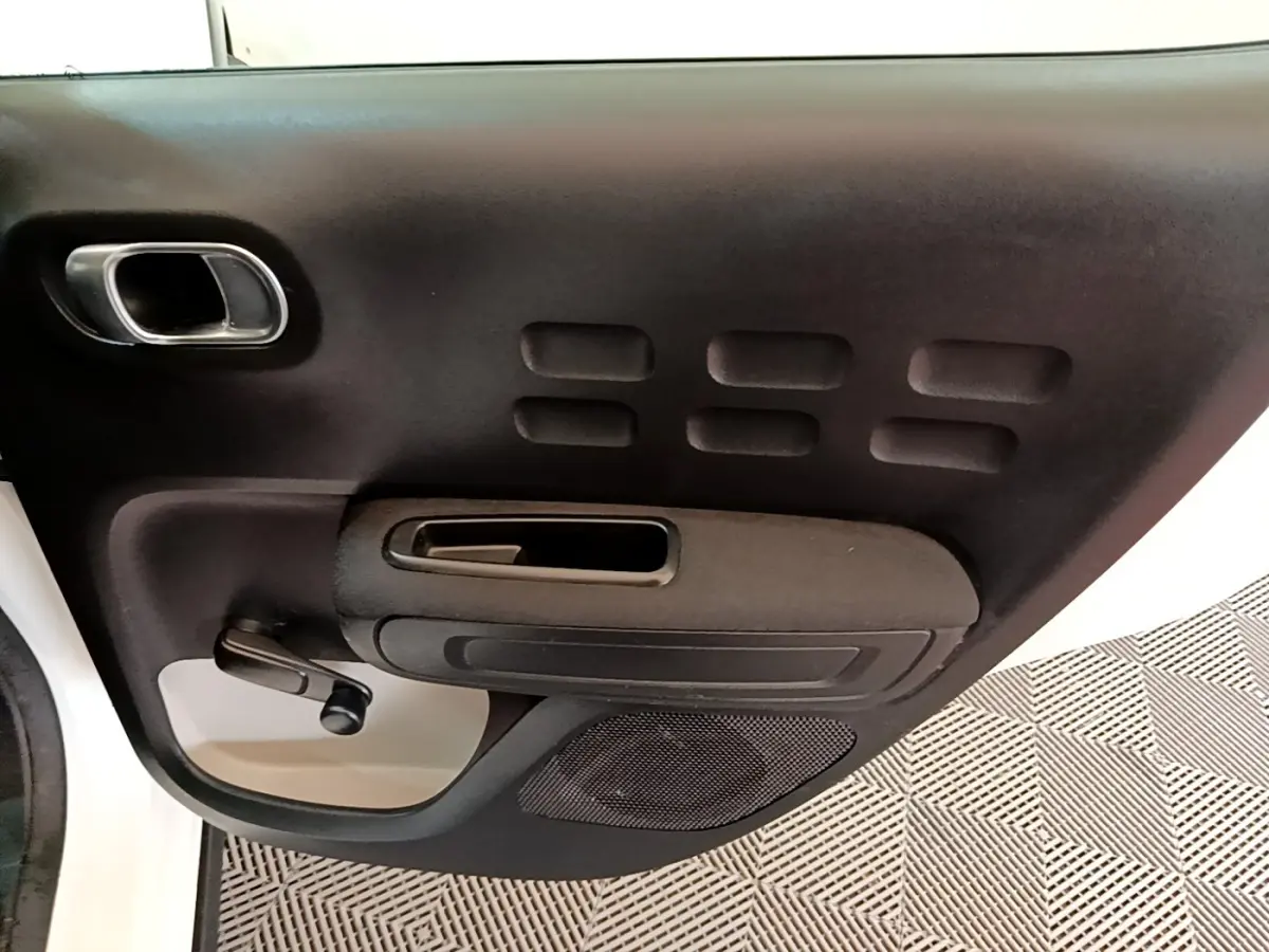 Gros plan sur la porte avant gauche noire avec poignée argentée et manivelle de vitre d'une Citroën C3 blanche.