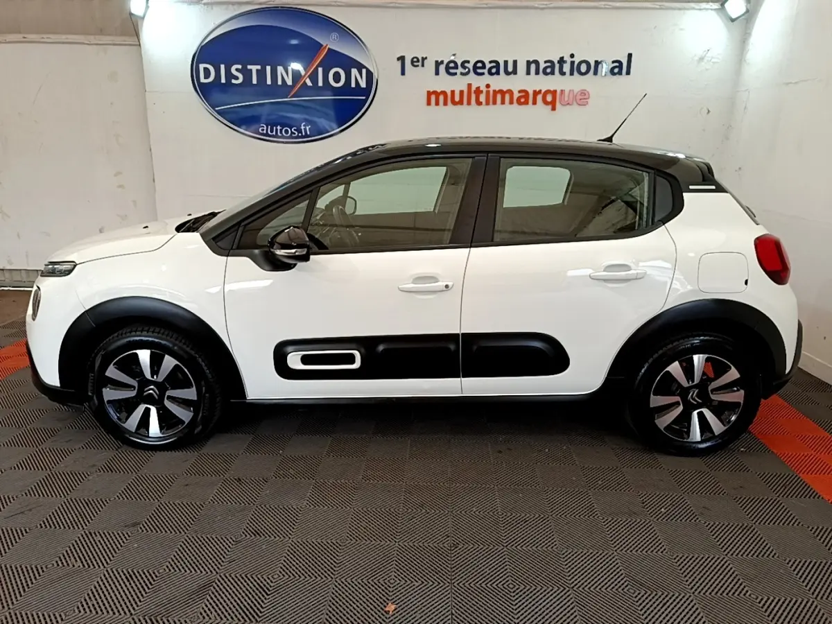 Vue de profil côté gauche d'une Citroën C3 blanche avec toit noir et protections latérales noires distinctives.