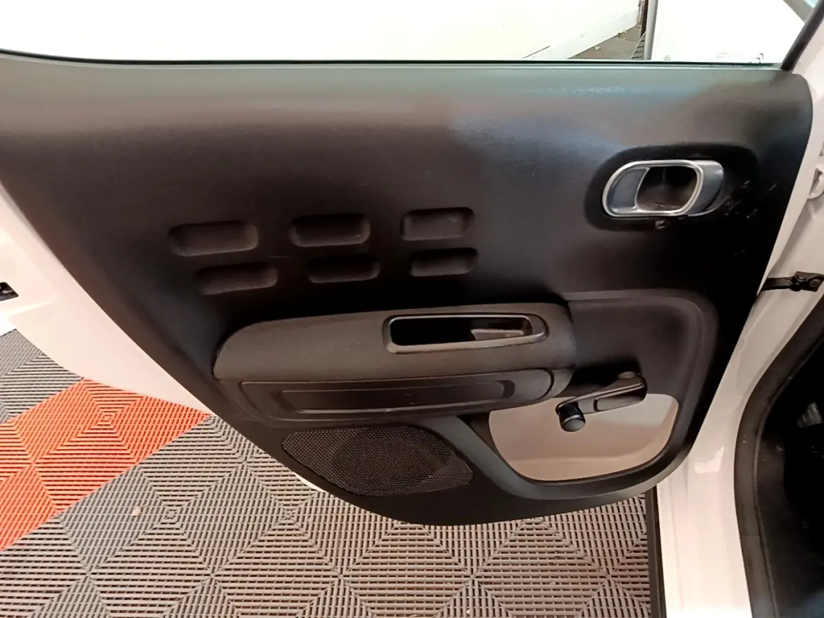 Vue intérieure de la porte avant gauche blanche d'une Citroën C3 2021 avec poignée et commande de vitre manuelle.