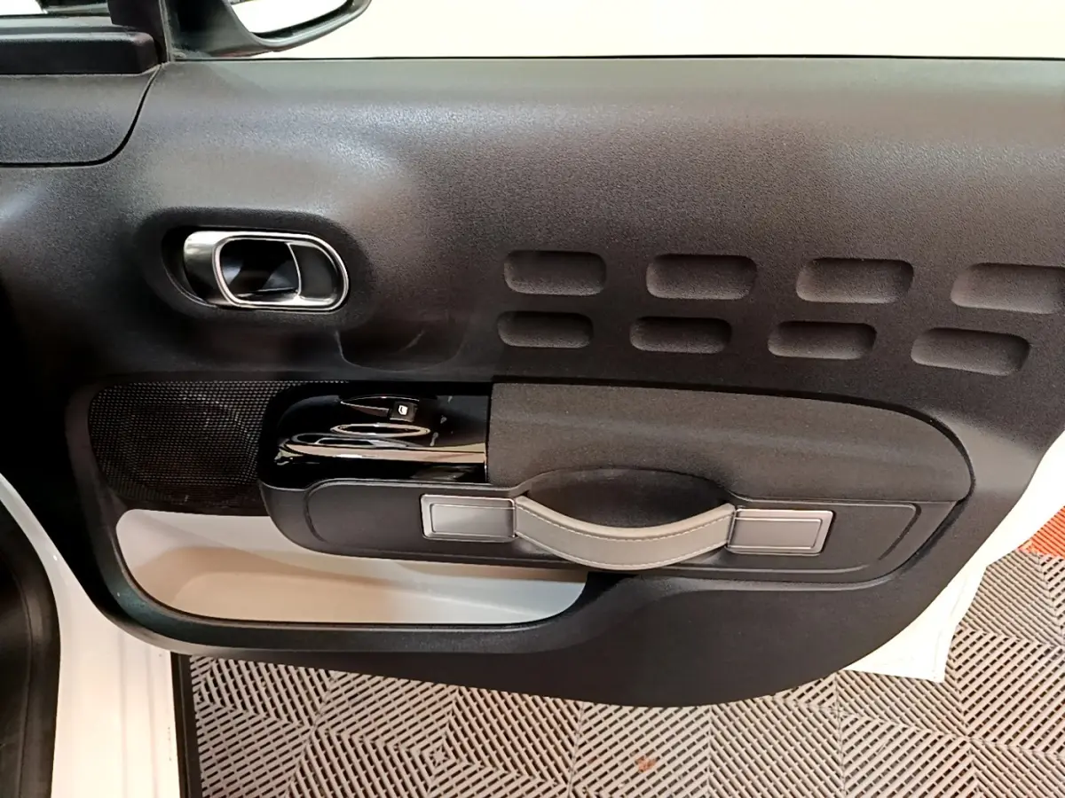 Vue rapprochée de la porte côté conducteur de la Citroën C3 blanche, mettant en valeur la poignée et les commandes de vitre.