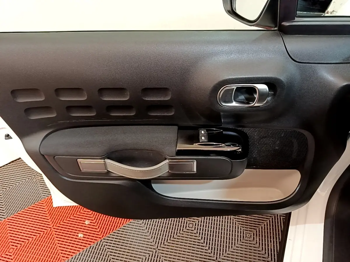 Vue intérieure de la porte avant gauche blanche de la Citroën C3 avec poignée noire et commandes électriques des vitres.
