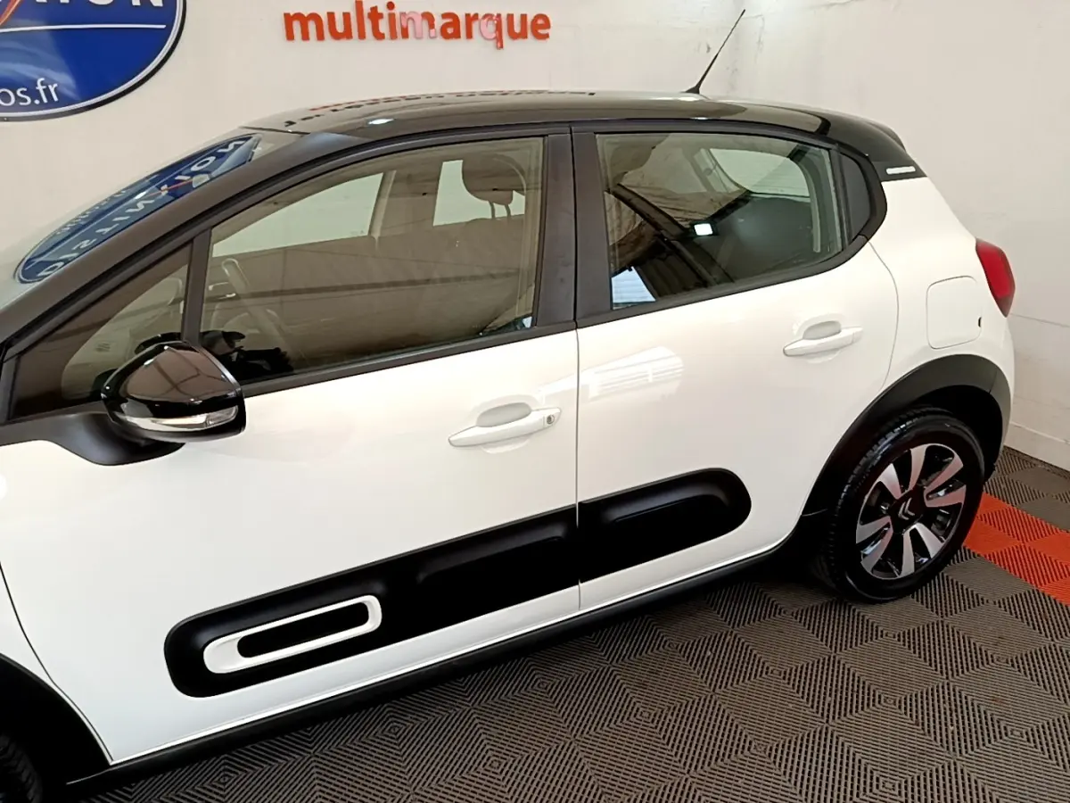 Vue de profil côté droit d'une Citroën C3 blanche avec toit noir et protections latérales noires distinctives.