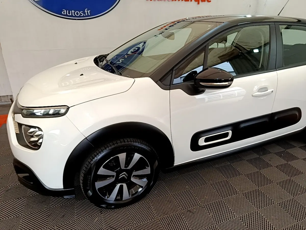 Vue 3/4 avant droit d'une Citroën C3 blanche 2021 avec protections latérales noires et jantes bicolores.