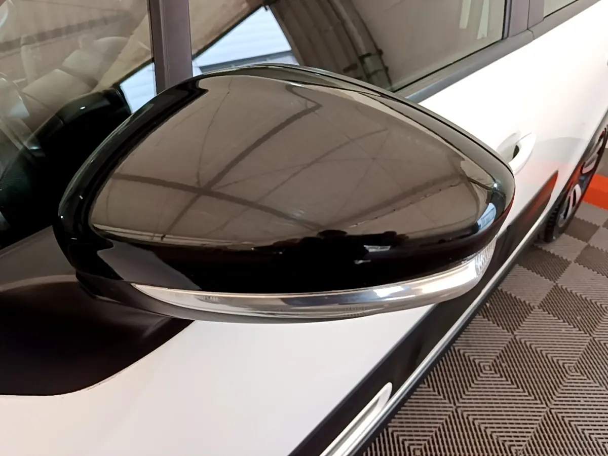 Gros plan sur le rétroviseur noir côté conducteur d'une Citroën C3 blanche, vue partielle du flanc avant droit.