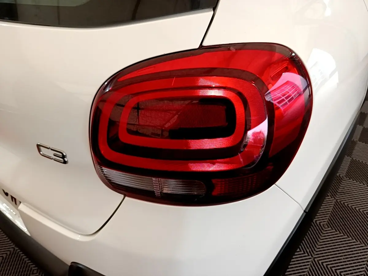Gros plan sur le feu arrière droit rouge et le logo C3 d'une Citroën C3 blanche vue de l'arrière.