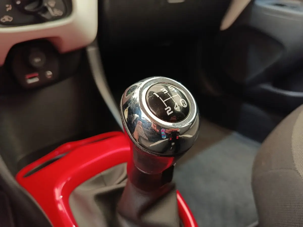 Gros plan sur le levier de vitesses manuel chromé de la Toyota Aygo 2016 avec contour rouge vif du pommeau.