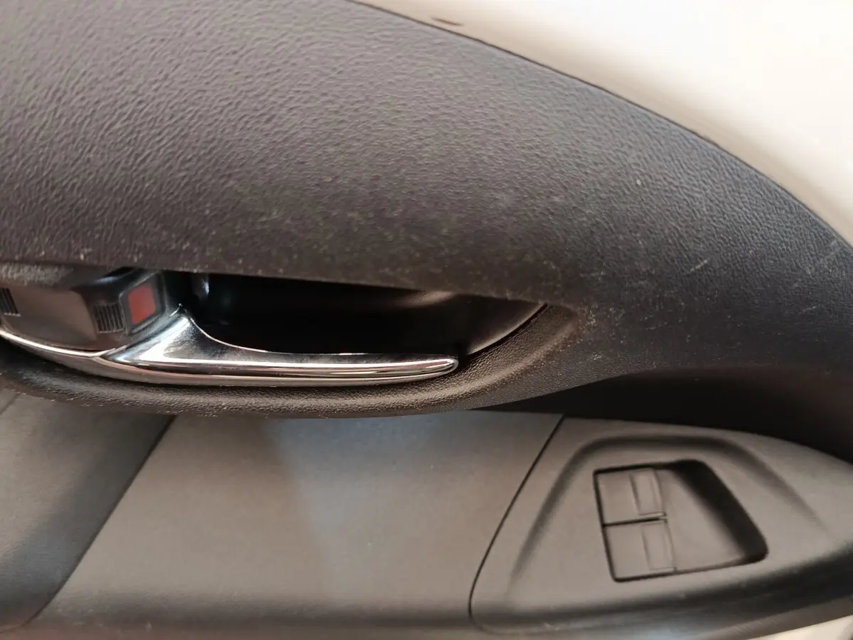 Poignée intérieure chromée et commandes des vitres électriques sur la porte côté conducteur d'une Toyota Aygo blanche.