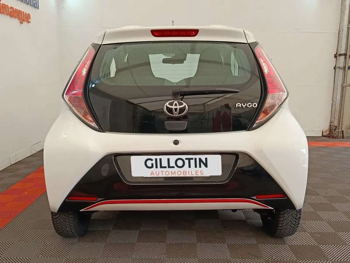 Vue arrière d'une Toyota Aygo blanche 2016 avec hayon noir et feux arrière triangulaires distinctifs.