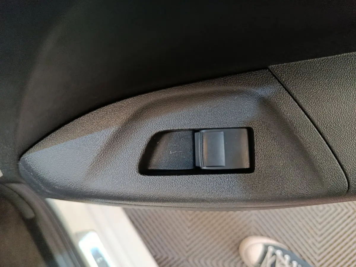 Gros plan sur l'interrupteur de verrouillage des portes côté conducteur d'une Toyota Aygo blanche, intérieur noir.