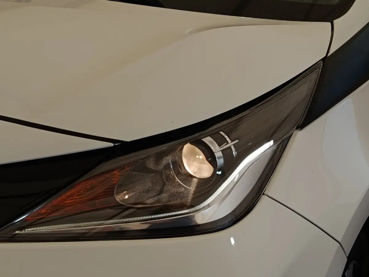 Gros plan sur le phare avant droit d’une Toyota Aygo blanche, mettant en valeur ses feux LED et détails du capot.
