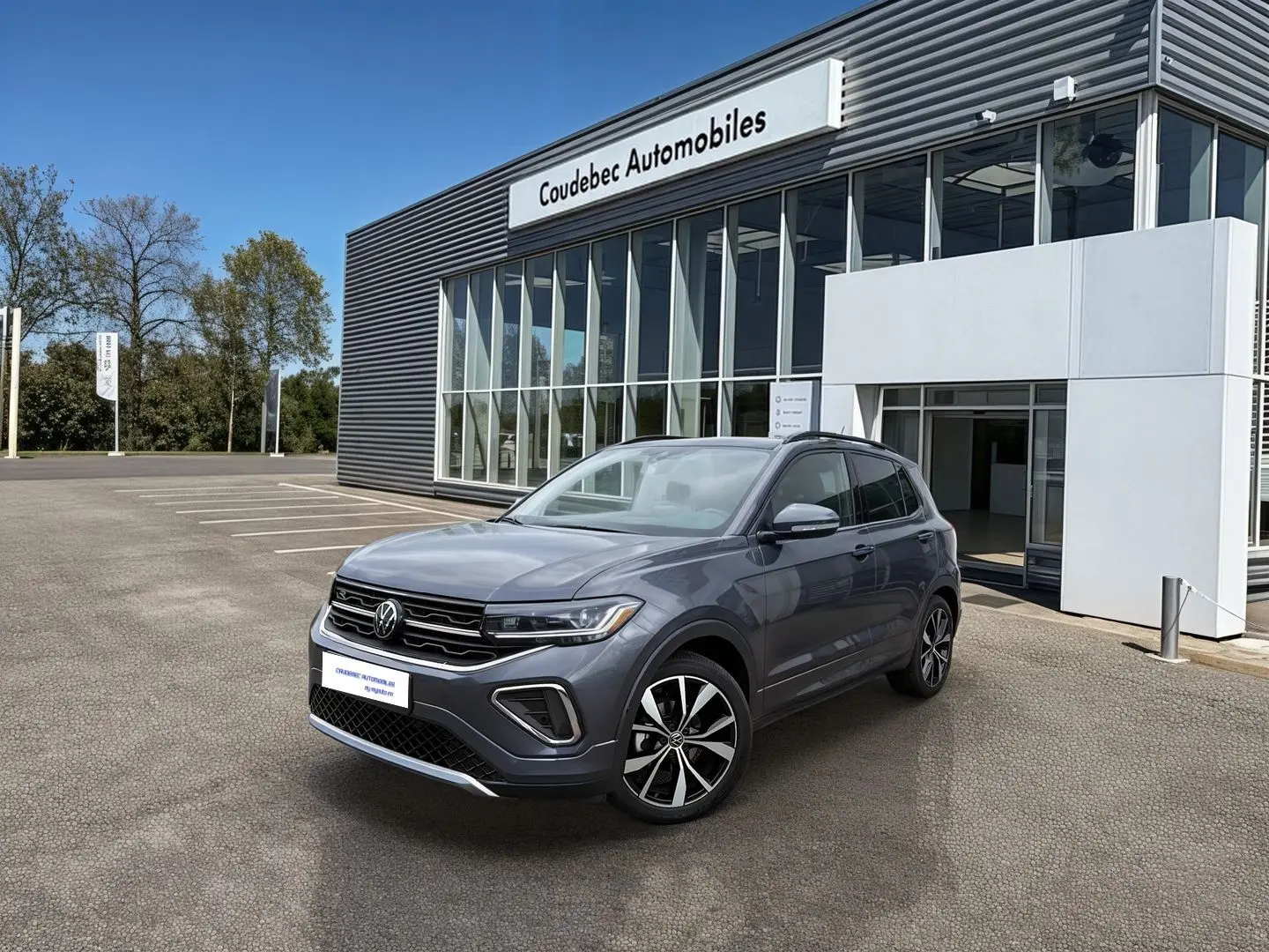 Volkswagen T-Cross gris en 3/4 avant droit, avec jantes alliage noires et grises, devant un bâtiment de concession.