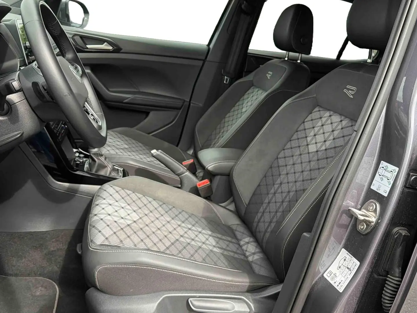 Vue intérieure côté droit sur les sièges avant gris à motif losange du Volkswagen T-Cross 2025 avec volant et levier de vitesse visibles.
