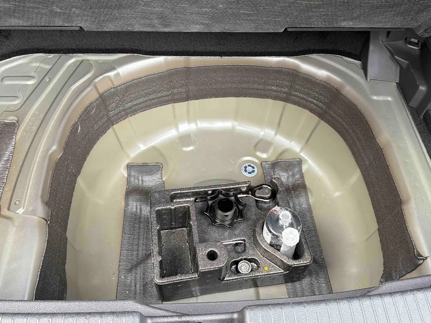 Vue plongeante sur le coffre ouvert d'un Volkswagen T-Cross gris, montrant le rangement sous la moquette.