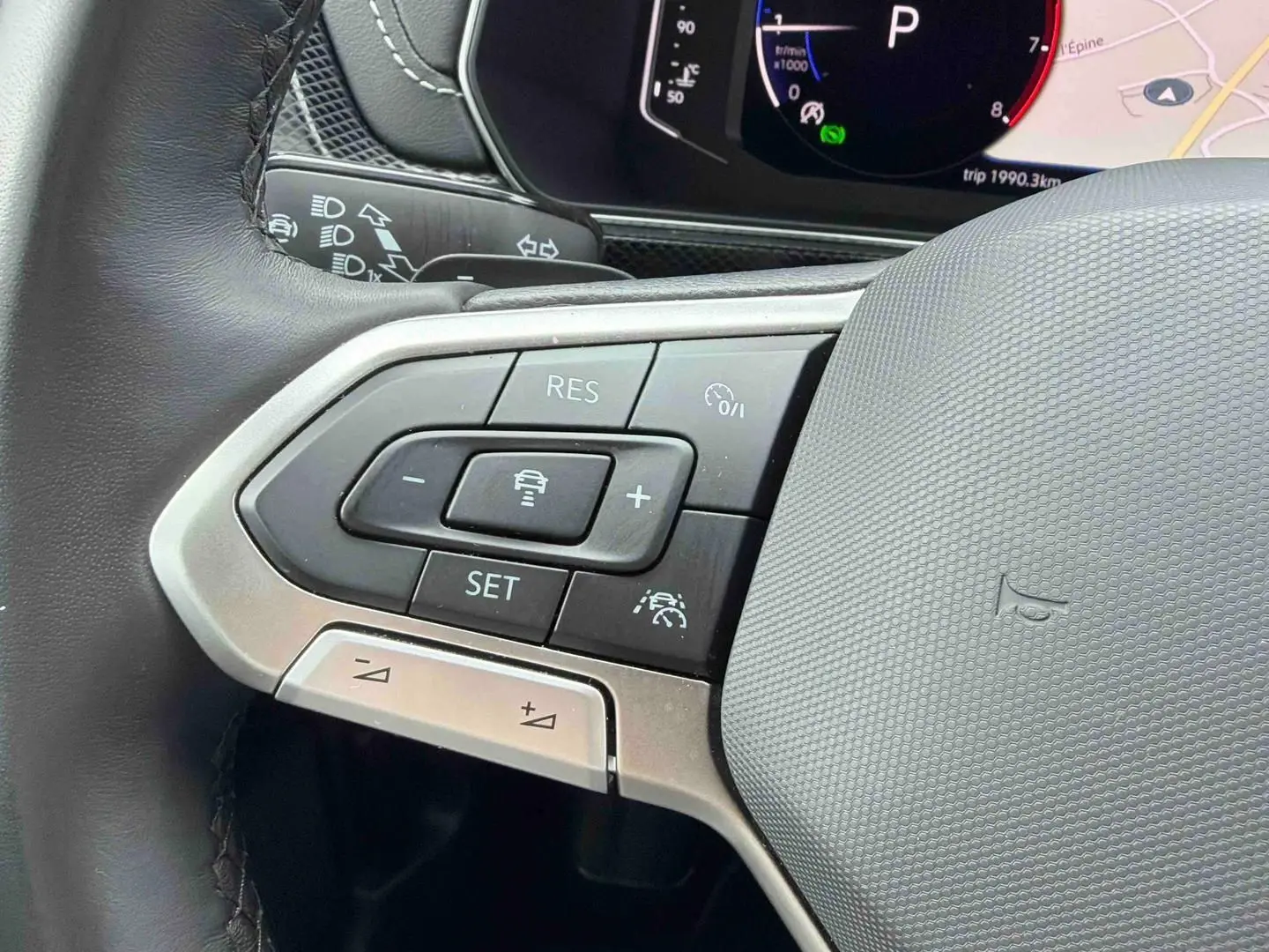Gros plan sur les commandes à gauche du volant cuir du Volkswagen T-Cross 2025, avec affichage digital en arrière-plan.