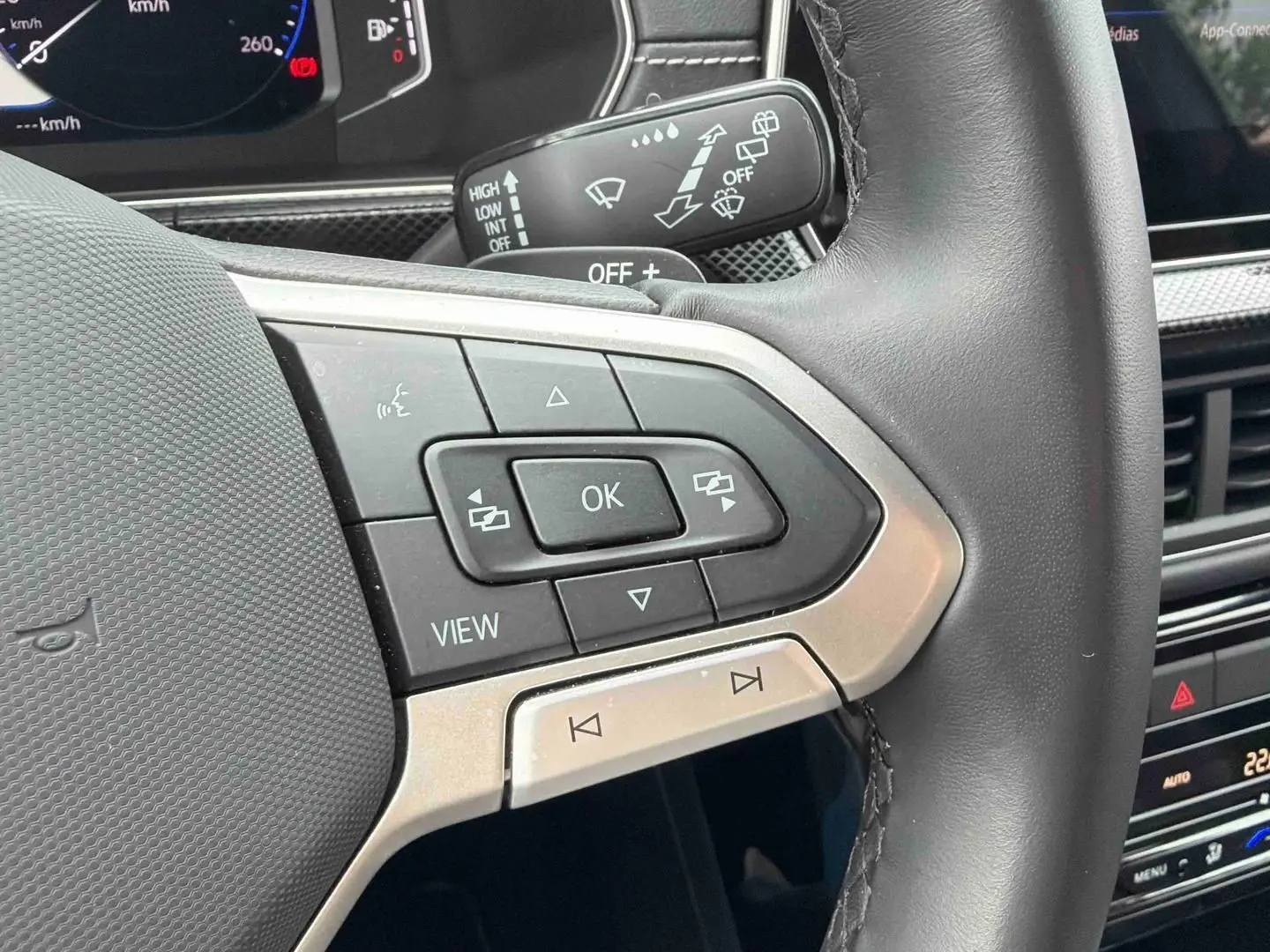 Gros plan sur les commandes multifonctions en cuir du volant du Volkswagen T-Cross, intérieur gris et tableau de bord numérique.