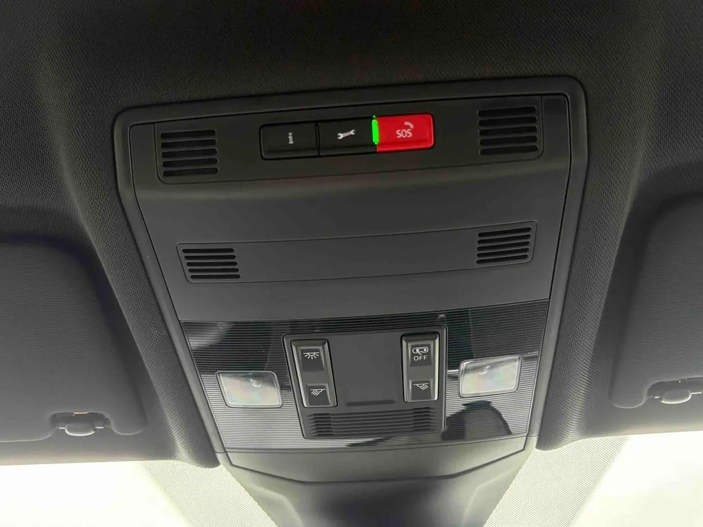 Vue en contre-plongée du panneau de commandes de toit intérieur du Volkswagen T-Cross gris, avec boutons SOS et éclairage.