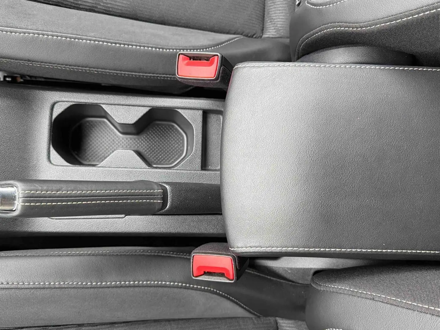 Vue rapprochée de la console centrale grise du Volkswagen T-Cross avec accoudoir, frein à main et ceintures rouges.
