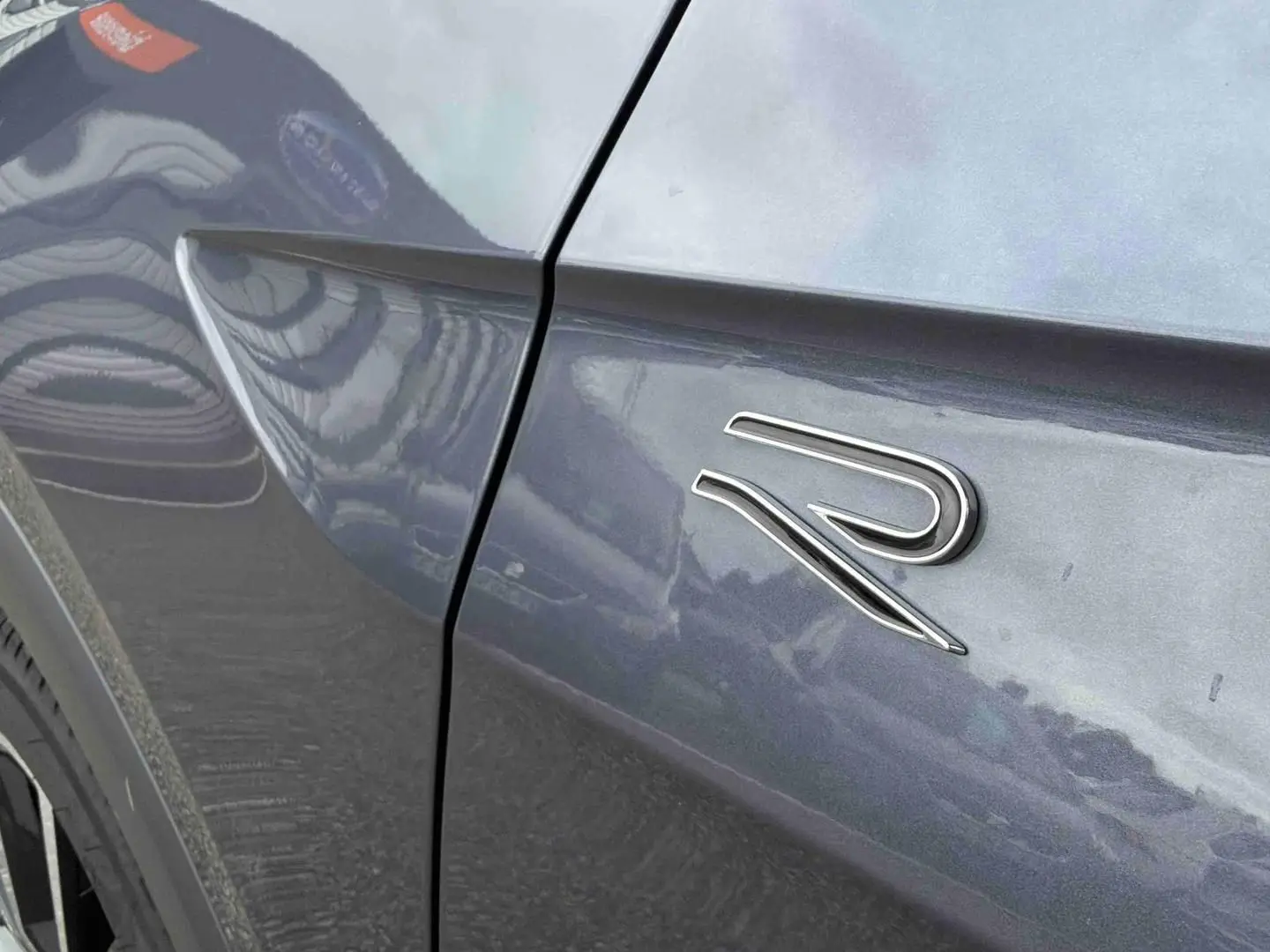 Détail de l'aile avant gauche grise d'un Volkswagen T-Cross avec logo R-Line chromé.