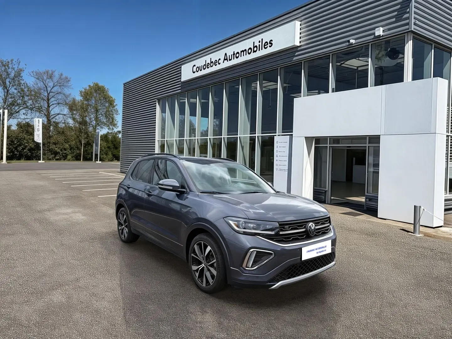 Vue 3/4 avant droite du Volkswagen T-Cross gris avec jantes alliage 18 pouces devant un concessionnaire.