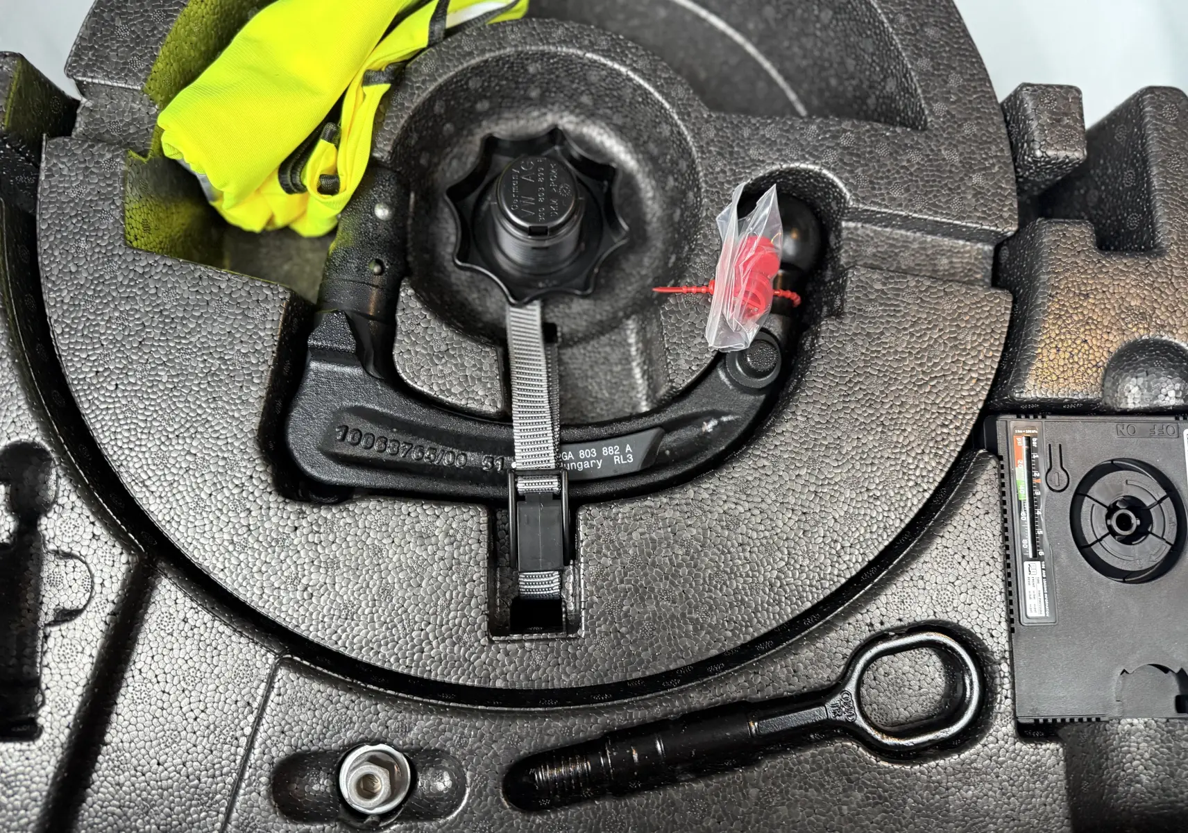 Gros plan sur le coffre à outils en mousse noire du Volkswagen T-Roc blanc, montrant le crochet de remorquage et un gilet jaune.