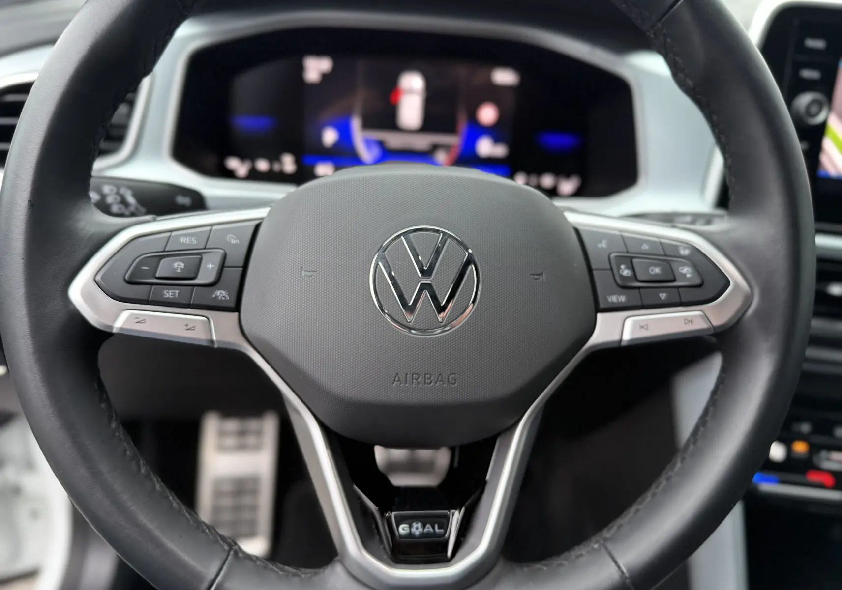 Gros plan sur le volant noir du Volkswagen T-Roc 2025, avec commandes intégrées et logo VW central argenté.