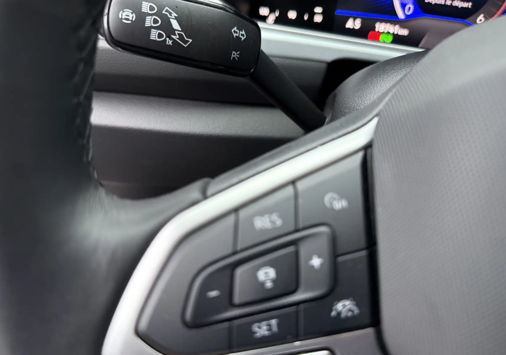 Gros plan sur les commandes au volant côté gauche du Volkswagen T-Roc 2025, avec tableau de bord numérique en arrière-plan.