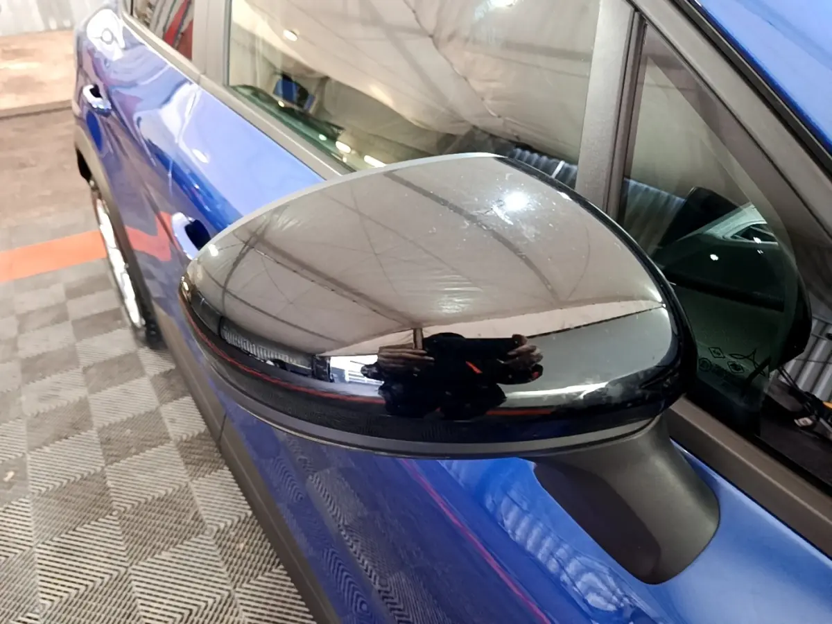 Gros plan sur le rétroviseur noir brillant côté conducteur du Renault Captur bleu, vue latérale gauche partielle.