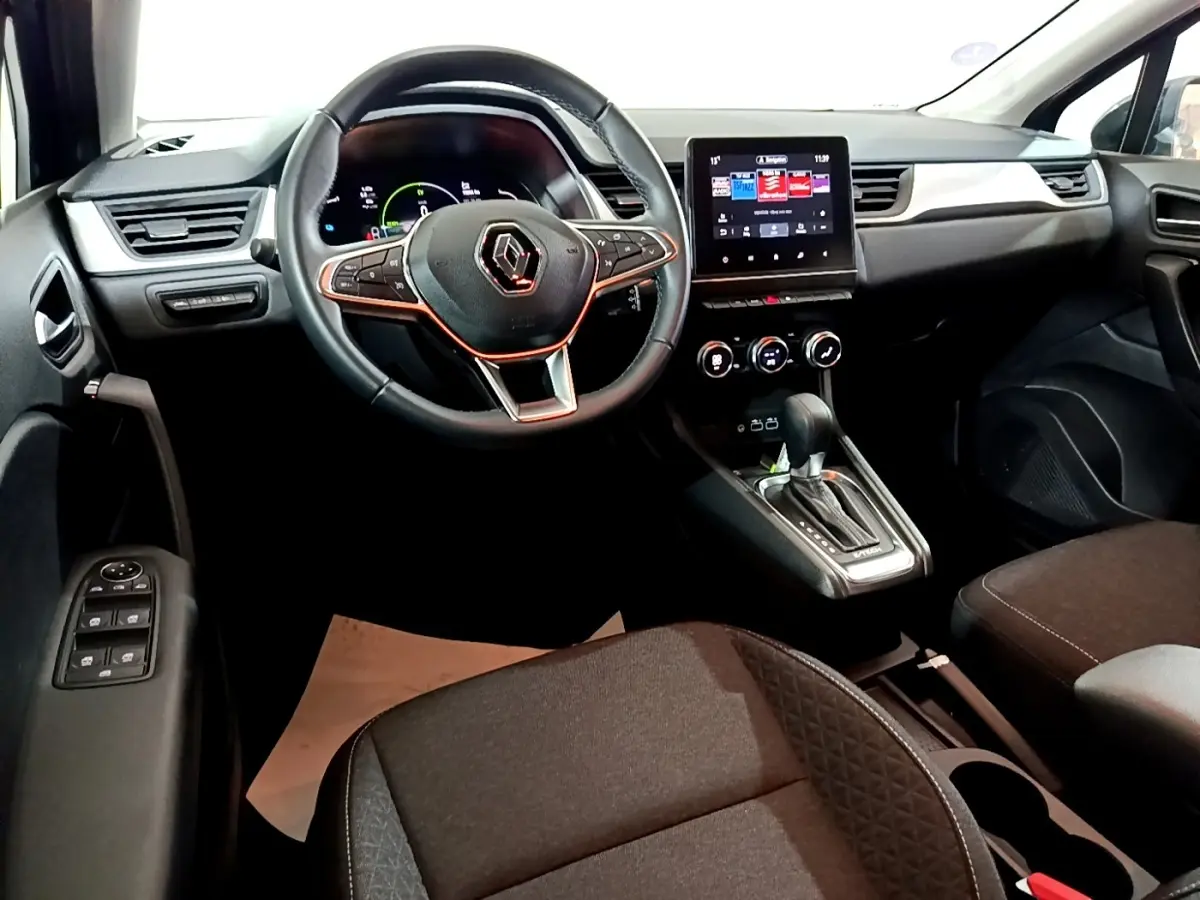 Vue intérieure avant du Renault Captur 2023, tableau de bord noir avec écran tactile central et volant multifonctions.