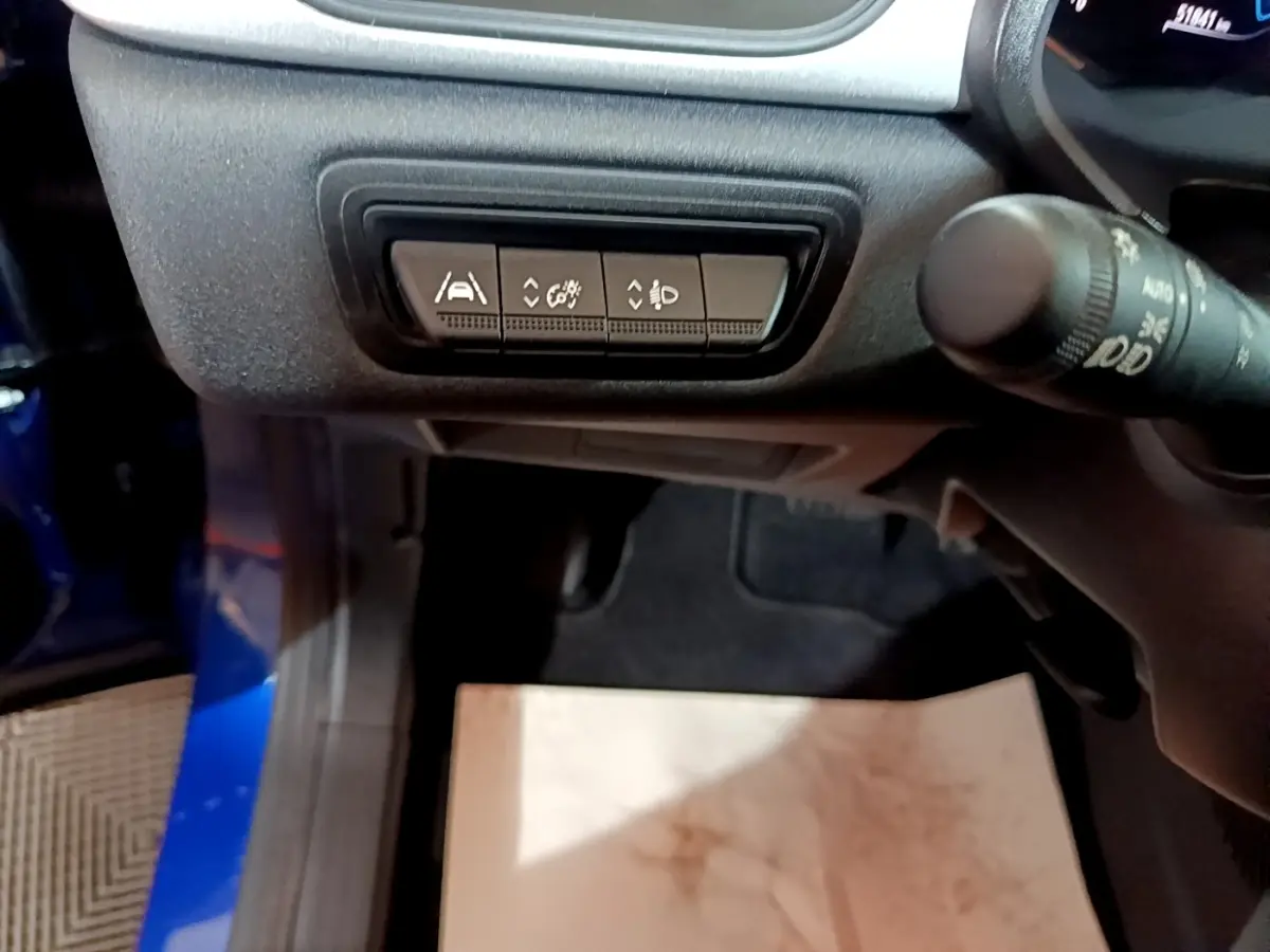 Vue intérieure côté conducteur du Renault Captur bleu, mettant en avant les boutons de réglage d'assistance et d'éclairage sous le tableau de bord.