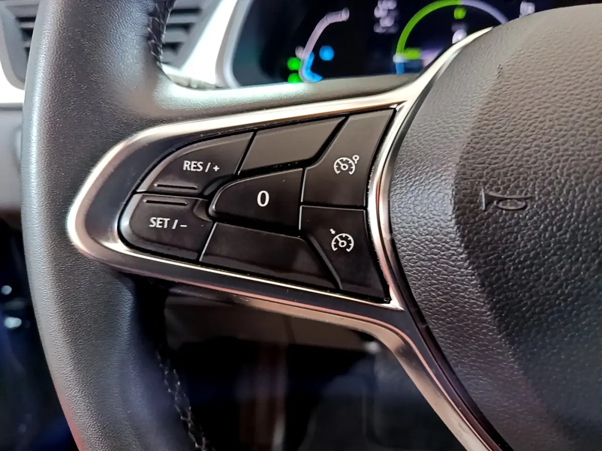Gros plan sur les commandes de régulateur de vitesse à gauche du volant noir du Renault Captur bleu hybride 2023.