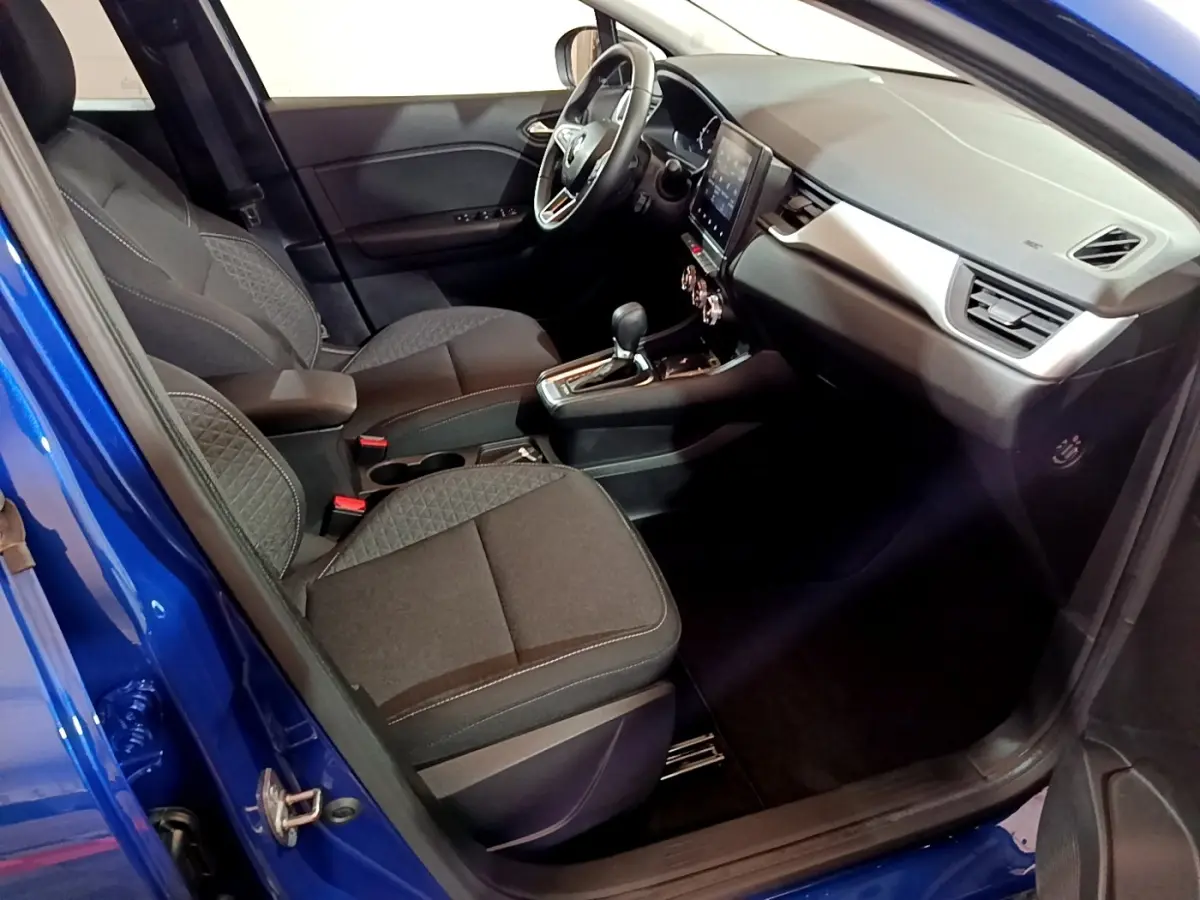 Vue intérieure côté conducteur du Renault Captur bleu 2023, avec sièges tissu noirs et tableau de bord moderne tactile.