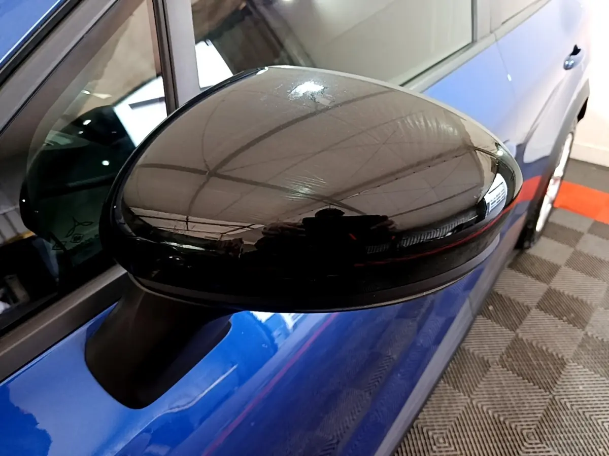 Gros plan sur le rétroviseur noir du côté gauche d'un Renault Captur bleu, avec reflet de l'environnement intérieur.