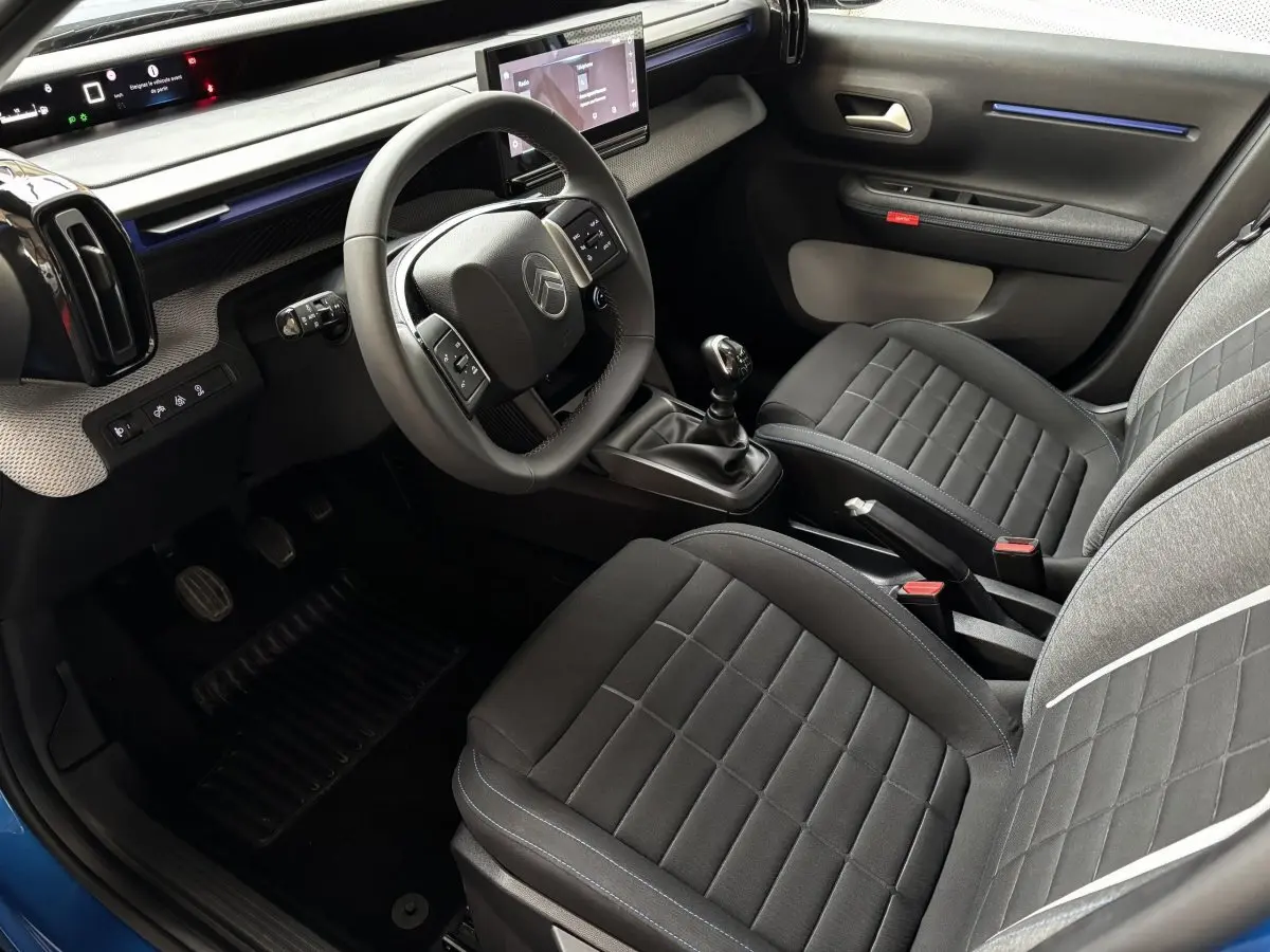 Vue intérieure côté conducteur de la Citroën C3 2025, volant cuir, sièges tissu noir et écran tactile central.