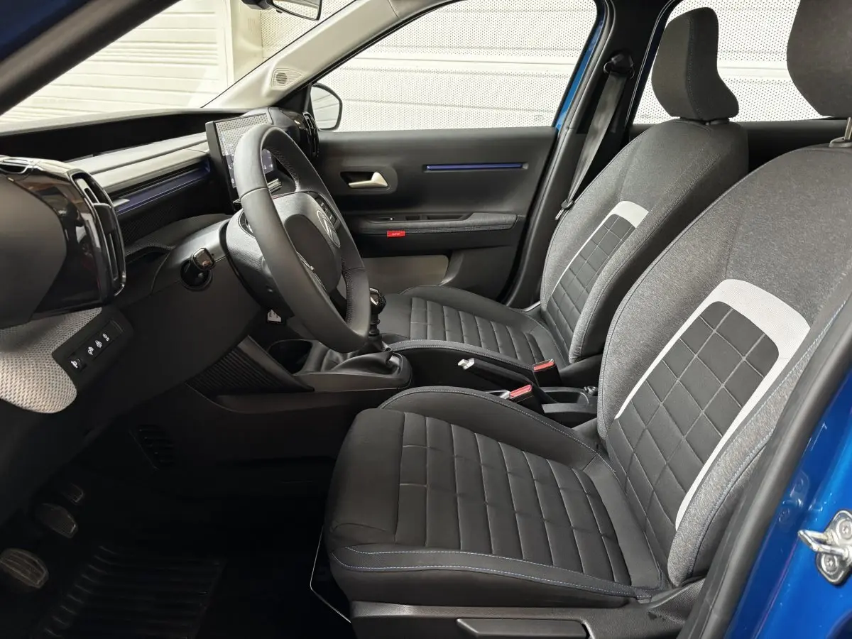 Intérieur de la Citroën C3 2025 vu côté conducteur, sièges tissu gris et noir avec surpiqûres bleues.