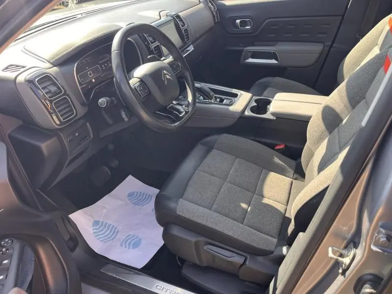 Vue intérieure côté conducteur du Citroën C5 Aircross gris, sièges tissu et cuir, volant multifonction et console centrale visible.